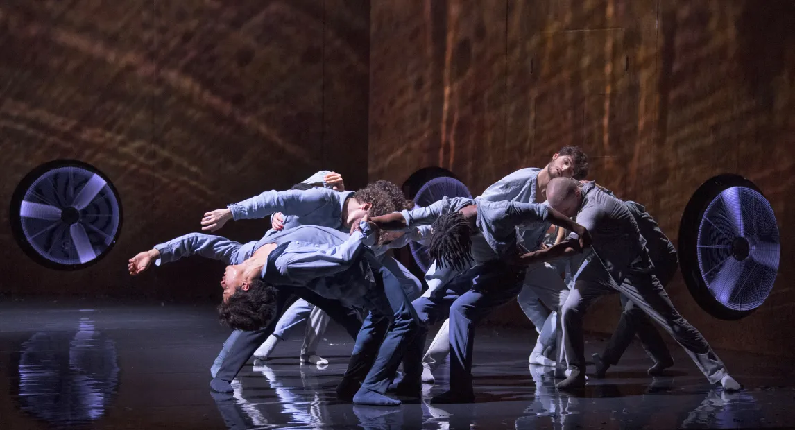 Un grupo de bailarines son iluminados por una luz desde arriba.