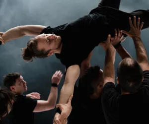 Un grupo de bailarines sostienen con sus manos en el aire a otro.