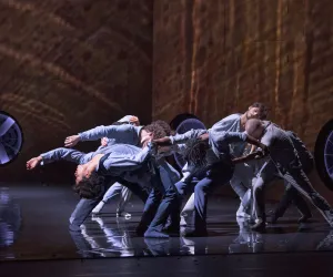 Un grupo de bailarines son iluminados por una luz desde arriba.